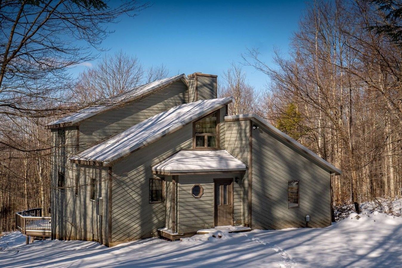 A wooden cabin with a steep roof, a front porch, and a snow-covered ground.