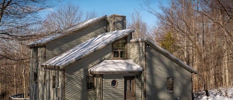 A wooden cabin with a steep roof, a front porch, and a snow-covered ground.