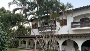 Un espace aménagé au bord d’une piscine à l’eau d’un bleu limpide, entouré d’un bâtiment blanc doté de nombreuses arcades et d’un toit recouvert de tuiles.