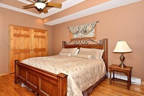 A bedroom with a wooden bed, a nightstand with a lamp, a ceiling fan, and a large wooden door.