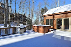 A wooden deck with a hot tub and a sauna, surrounded by snow-covered trees.