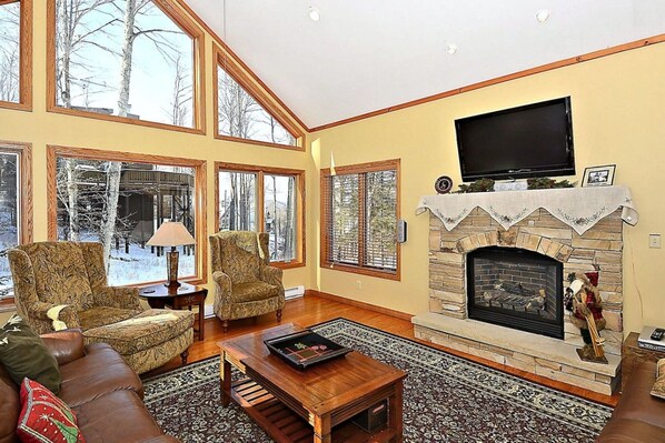 A spacious living room with a fireplace, large windows, and a television.
