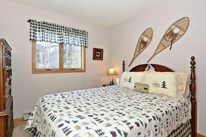 Un dormitorio con cama, una ventana con cortina a cuadros, una lámpara de pared y un adorno en la pared.