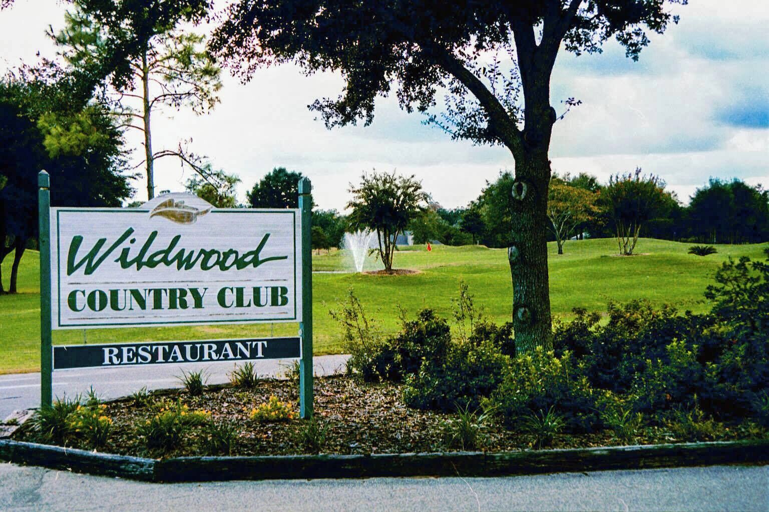 A sign for Wildwood Country Club Restaurant with a view of a well-maintained lawn and trees.
