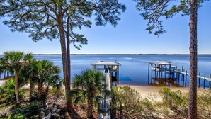 A beach with wooden walkways leading to covered structures, surrounded by pine trees and palm plants. - "Bayside Retreat" Panacea FL...Bay Front, Dock, 2 Large Porches, No Pets, Wifi (Panacea)