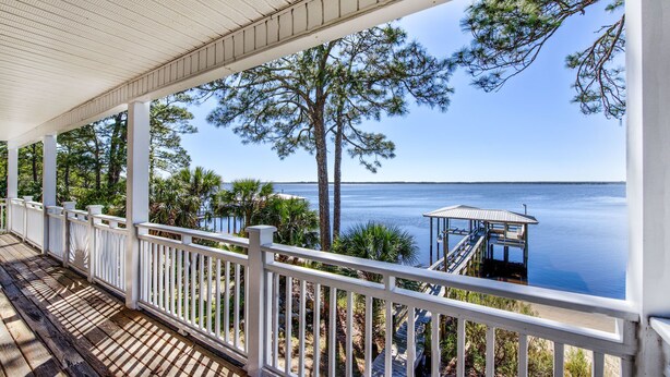 A covered wooden deck with white railings overlooking a calm body of water, a dock, and a small gazebo. - "Bayside Retreat" Panacea FL...Bay Front, Dock, 2 Large Porches, No Pets, Wifi (Panacea)