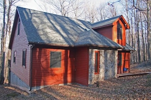 A two-story log cabin with a stone foundation, a red exterior, and a steeply pitched roof.