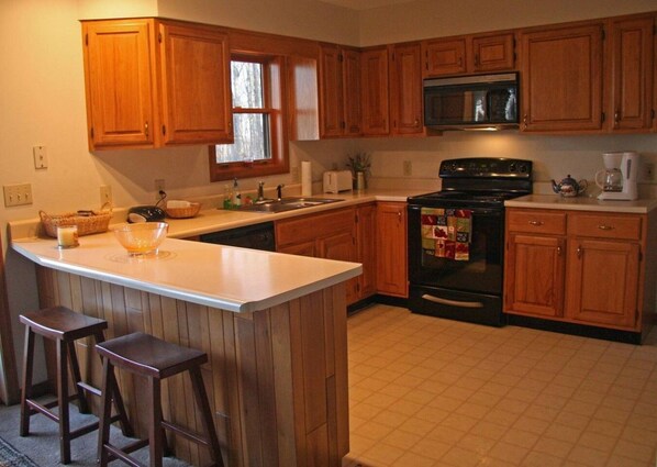 A kitchen with wooden cabinets, a stove, a microwave, and a coffee maker.