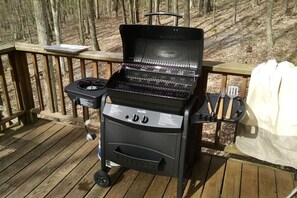 A portable grill with a side burner and a built-in thermometer, placed on a wooden deck.