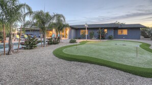 A modern house with a well-maintained lawn, a pool, and a tennis court.