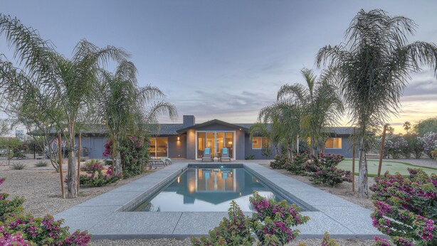 A modern house with a swimming pool, surrounded by palm trees and flowering plants.