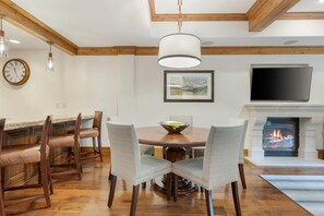 Un coin repas comprenant une table en bois, des chaises, une horloge, une cheminée et un téléviseur.