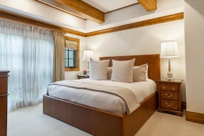 A bedroom with a large bed, wooden headboard, bedside tables with lamps, and a window with curtains.