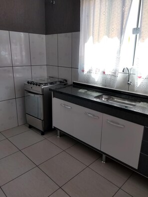 Een koelkast, een oven, een kookplaat, kookgerei, borden en bestek