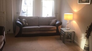 Een woonkamer met een bank, een lamp, een vaas en een schilderij aan de muur.