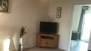 Een woonkamer met een flatscreen televisie op een houten kast, een potplant en een grote bank.