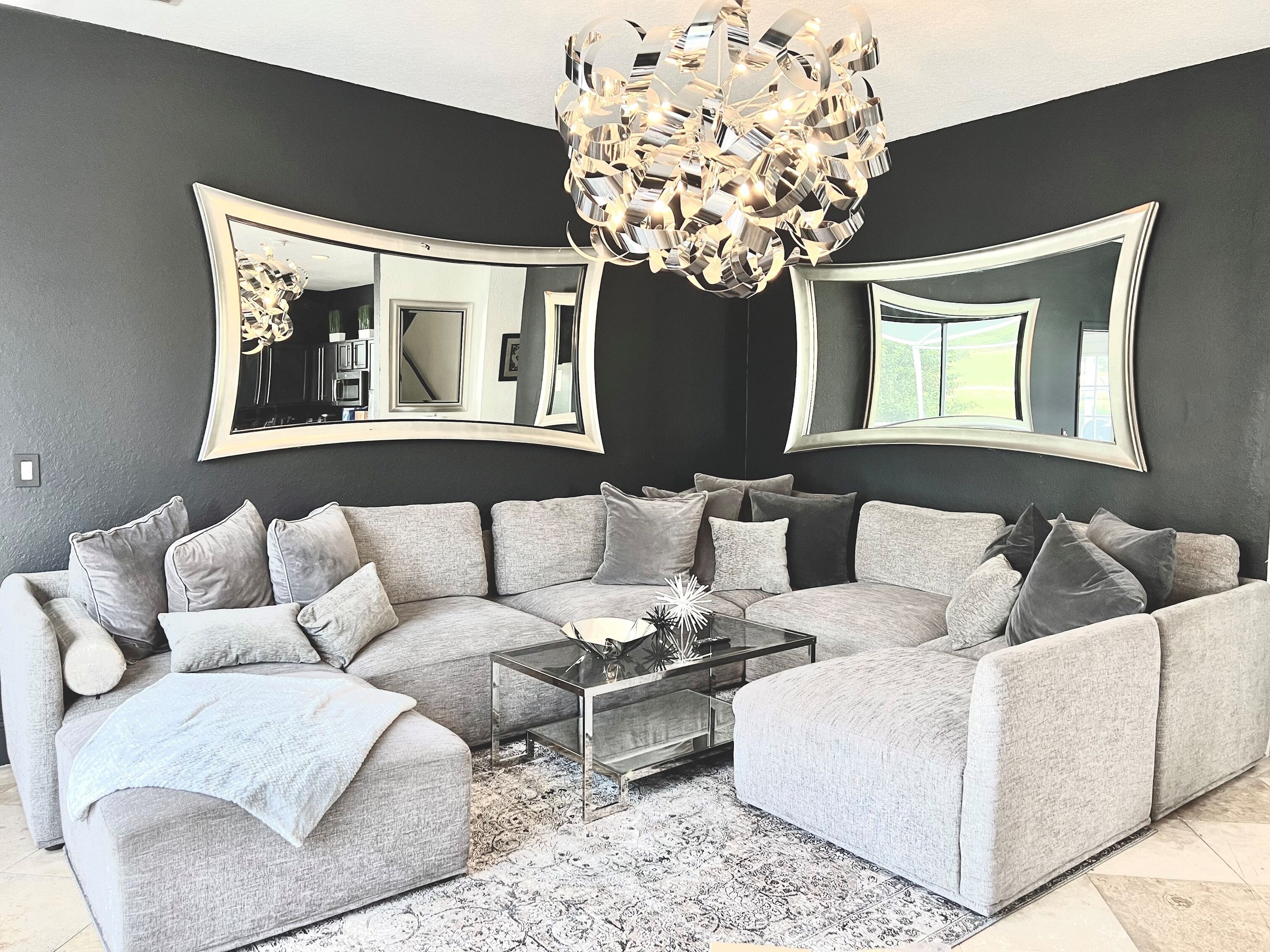 A modern living room with a grey sectional sofa, a glass coffee table, and a large chandelier.