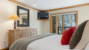 A bedroom with a bed, a dresser, a television, and a window with a view of trees. - Riva Ridge 715 | 2BR Vail Village (Vail)