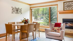 A dining area with a wooden table and chairs, a vase with flowers, and a fireplace with a fire. - Riva Ridge 715 | 2BR Vail Village (Vail)