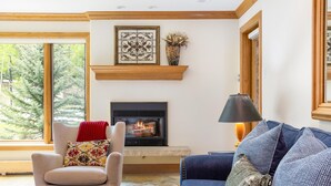 A living room with a fireplace, a sofa, a chair, and a window with a view of trees. - Riva Ridge 715 | 2BR Vail Village (Vail)