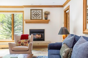 A living room with a fireplace, a sofa, a chair, and a window with a view of trees.