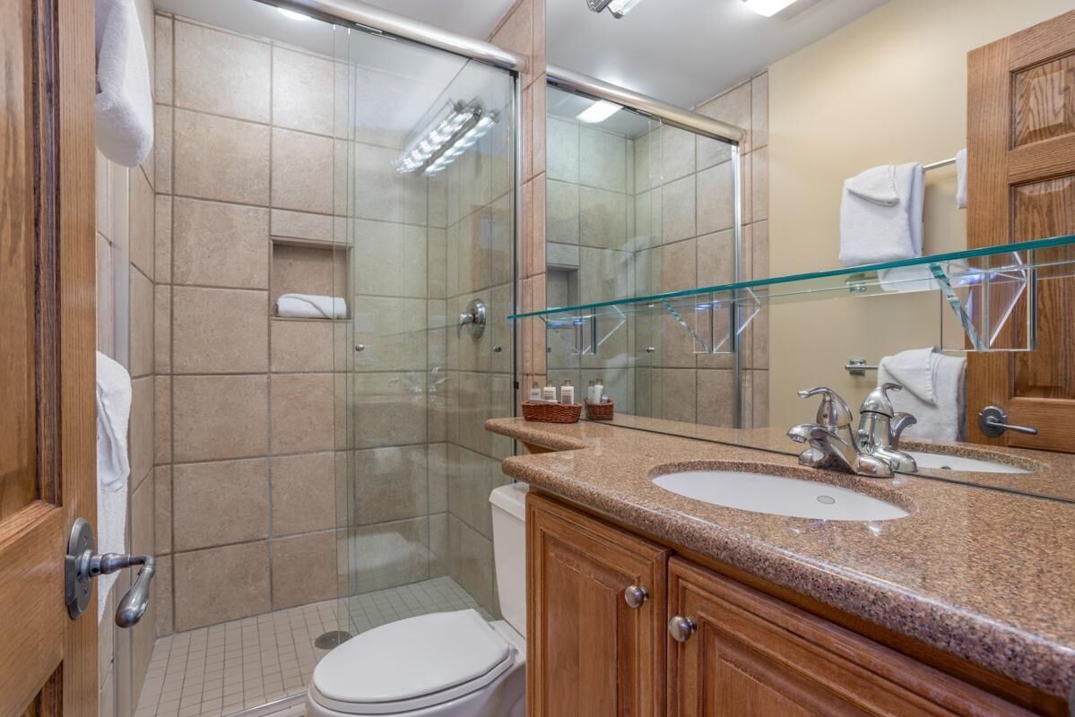 A modern bathroom with a glass-enclosed shower, a white toilet, and a granite countertop sink with a mirror.