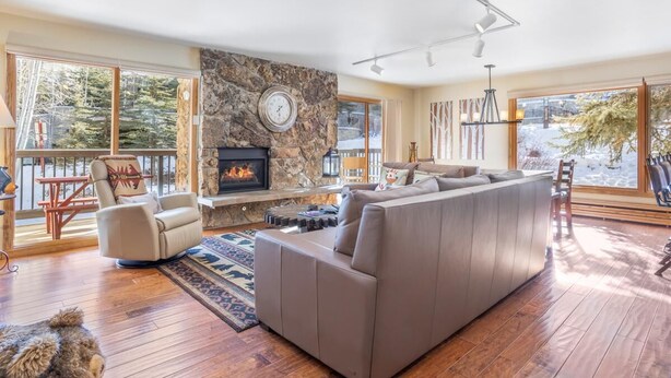 A spacious living room with a large sectional sofa, a stone fireplace, and a view of the outdoors. - Riva Ridge 655 | 2BR Vail Village (Vail)
