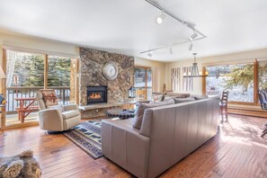 A spacious living room with a large sectional sofa, a stone fireplace, and a view of the outdoors. - Riva Ridge 655 | 2BR Vail Village (Vail)