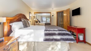 A hotel room with a bed, a wooden headboard, a red nightstand, a television, and a view of the outside. - Riva Ridge 655 | 2BR Vail Village (Vail)