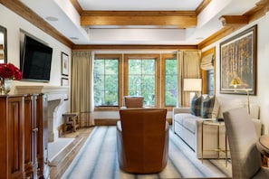 A living room with a sofa, armchair, wooden cabinet, TV, and large windows with curtains. - Willows 401 | Luxury 2BR Vail Village (Vail)
