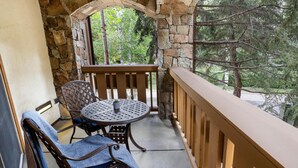 Ein Balkon mit Steinmauer, Holzgeländer, einem runden Tisch und zwei Stühlen.