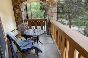 A balcony with a stone wall, a wooden railing, a round table, and two chairs. - Willows 401 | Luxury 2BR Vail Village (Vail)
