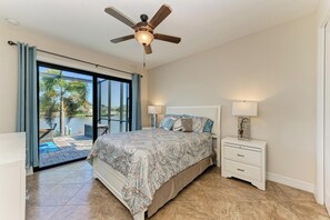 Une chambre à coucher avec un lit, des tables de chevet, un ventilateur de plafond et une vue sur une piscine, visible à travers une porte vitrée.