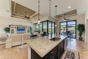 A spacious living area with a large island, a seating area with a TV, and a patio with outdoor furniture.