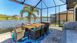 A covered outdoor patio with a table and chairs, a grill, and a view of a water body. - WATERFRONT LUXURY PRIVATE HEATED POOL&SPA/MIN TO BEACH/DOCK&LIFT/GULF ACCESS (Port Charlotte)