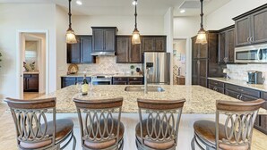 A kitchen with granite countertops, dark wooden cabinets, stainless steel appliances, and four barstools. - WATERFRONT LUXURY PRIVATE HEATED POOL&SPA/MIN TO BEACH/DOCK&LIFT/GULF ACCESS (Port Charlotte)