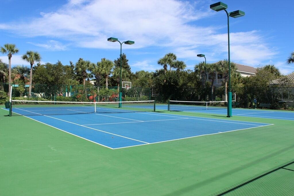 En utomhusbana för tennis med gröna och blå ytor, omgiven av palmer och en klar himmel.