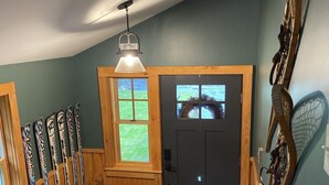 A wooden staircase leading to a door with a window, a wall-mounted ski rack, and a ceiling light fixture. - Quiet, Peaceful Location, Walk to Everything, Hot Tub, Fireplace, Game Room (Lake Placid)