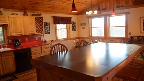 A wooden interior with a large island table, wooden cabinets, and pendant lighting. - Quiet, Peaceful Location, Walk to Everything, Hot Tub, Fireplace, Game Room (Lake Placid)
