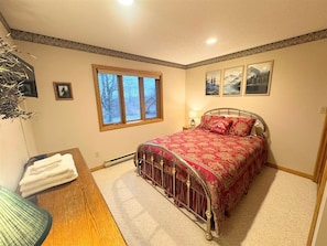 A bedroom with a metal bed frame, a window with a view, a bedside table with a lamp, and a wall-mounted picture. - Serenity - Access to Swimming & Fishing Pond (Davis)