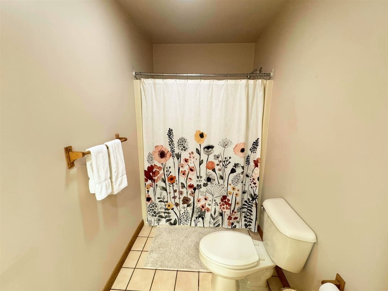 Une salle de bain comprenant des toilettes, un rideau de douche à motifs floraux et un porte-serviettes avec deux serviettes.