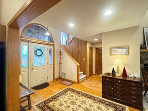 A spacious living area with a staircase, wooden flooring, a fireplace, and a large rug.