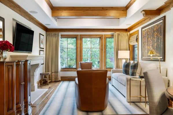 A living room with a sofa, armchair, wooden cabinet, TV, and large windows with curtains.