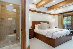 A bedroom with a large bed, a nightstand, a wooden headboard, a glass shower enclosure, and a window with curtains.