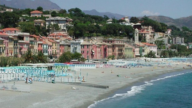 Une plage côtière avec des bâtiments aux couleurs vives en arrière-plan et une étendue de sable bordée de parasols.