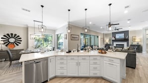 Cocina moderna con isla central, muebles blancos e iluminación colgante.