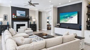 Una sala de estar moderna con chimenea, un televisor de pantalla plana grande y un ventilador de techo.