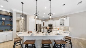 Una cocina moderna con armarios blancos, una isla grande con taburetes e iluminación colgante.