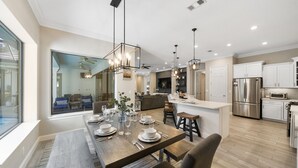 Cocina moderna con armarios blancos, un refrigerador de acero inoxidable y un comedor con una mesa de madera para cuatro personas.