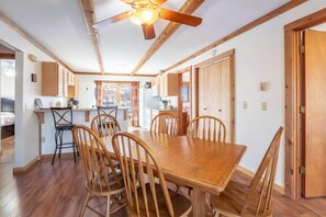 Uma sala de jantar com mesa e cadeiras de madeira, um ventilador de teto e paredes de madeira.
